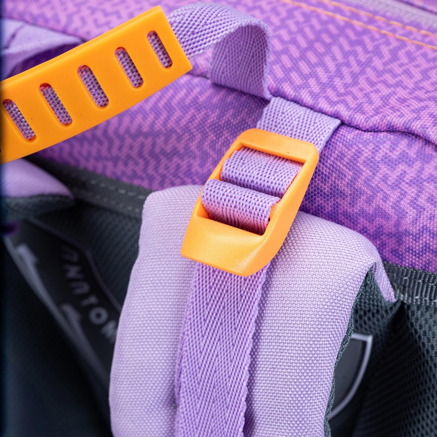 Backpack shoulder strap close-up in lilac purple with orange plastic adjustment buckles and textured chevron fabric panel