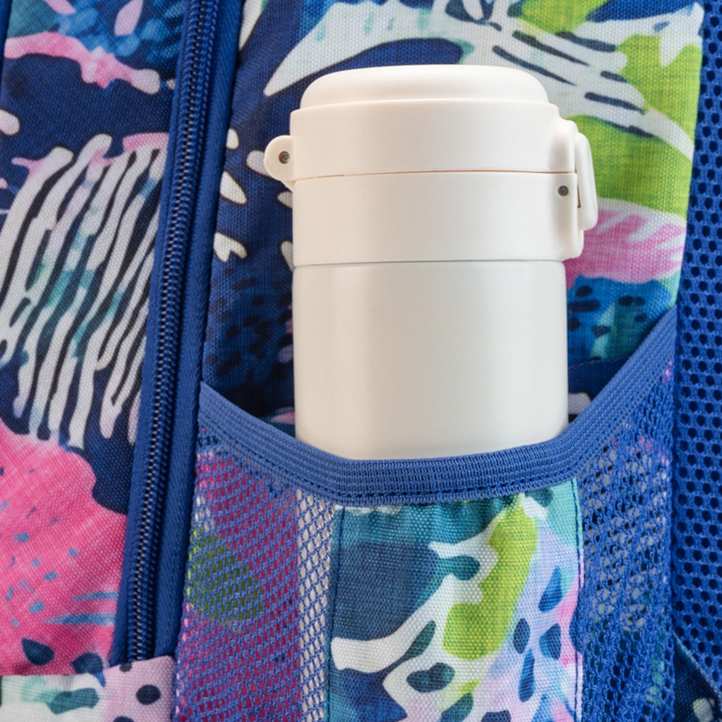 White insulated food thermos jar with clip-lock lid in mesh side pocket of blue tropical print backpack