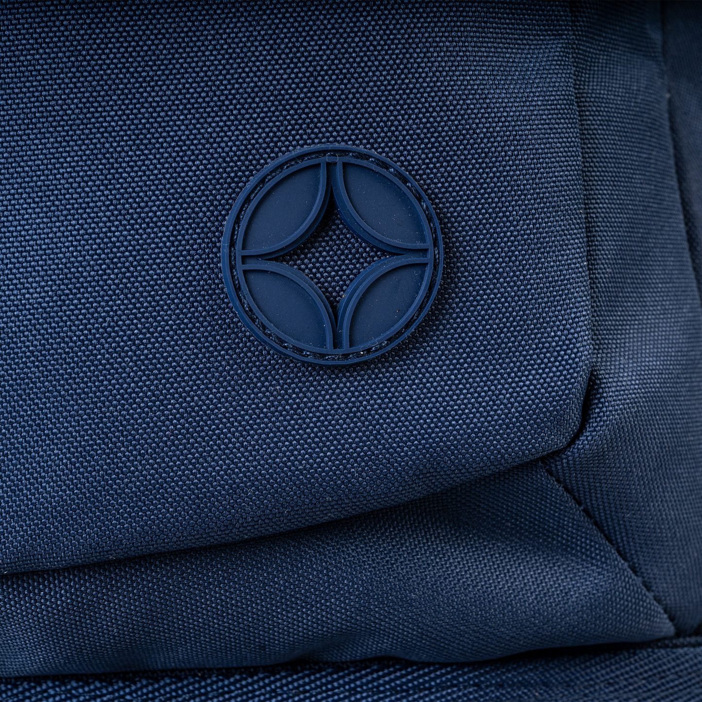 Navy blue nylon bag close-up showing circular rubber logo badge with four-petal geometric design on textured fabric surface