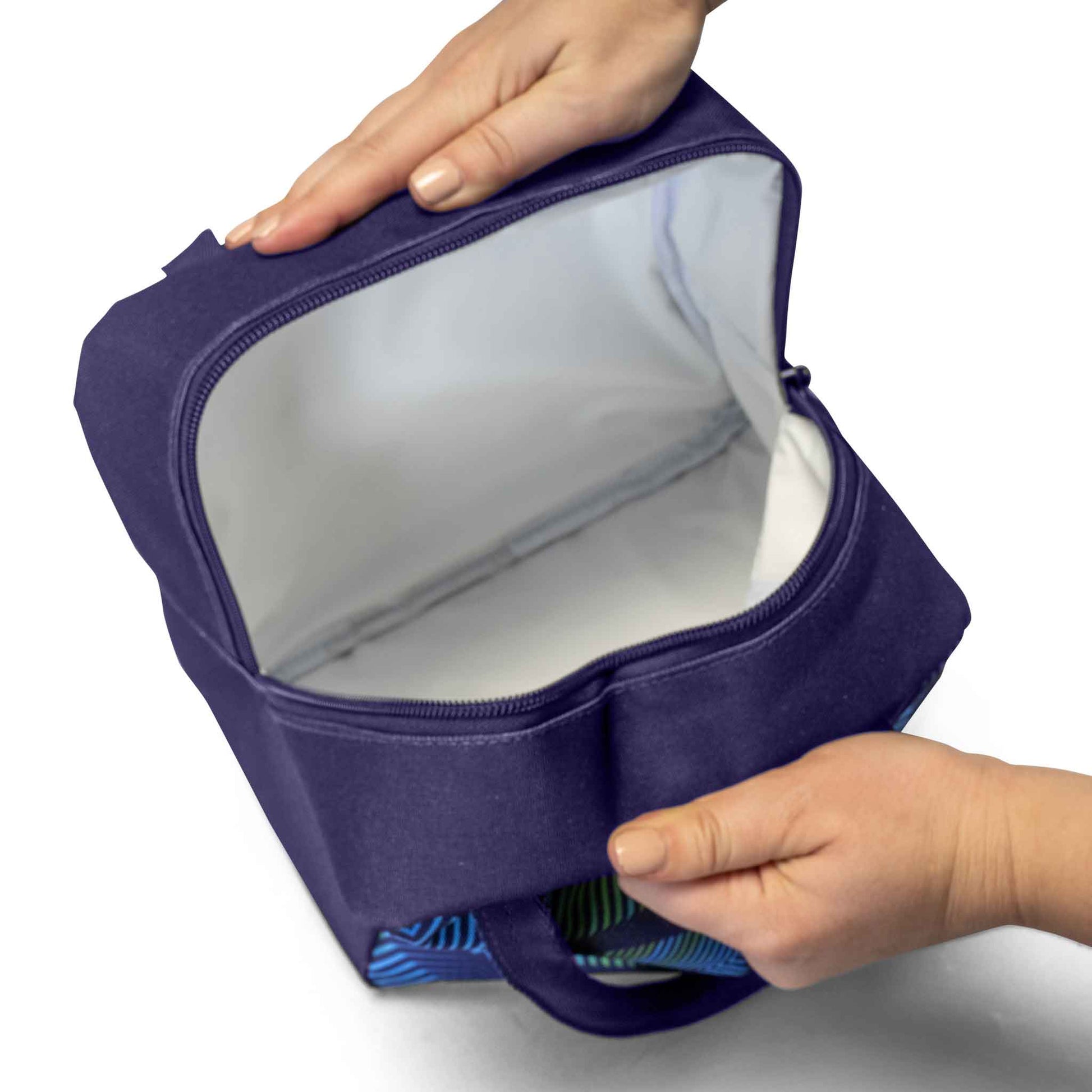 Navy blue insulated lunch bag open to show white interior lining with blue and green patterned carry handle held by two hands
