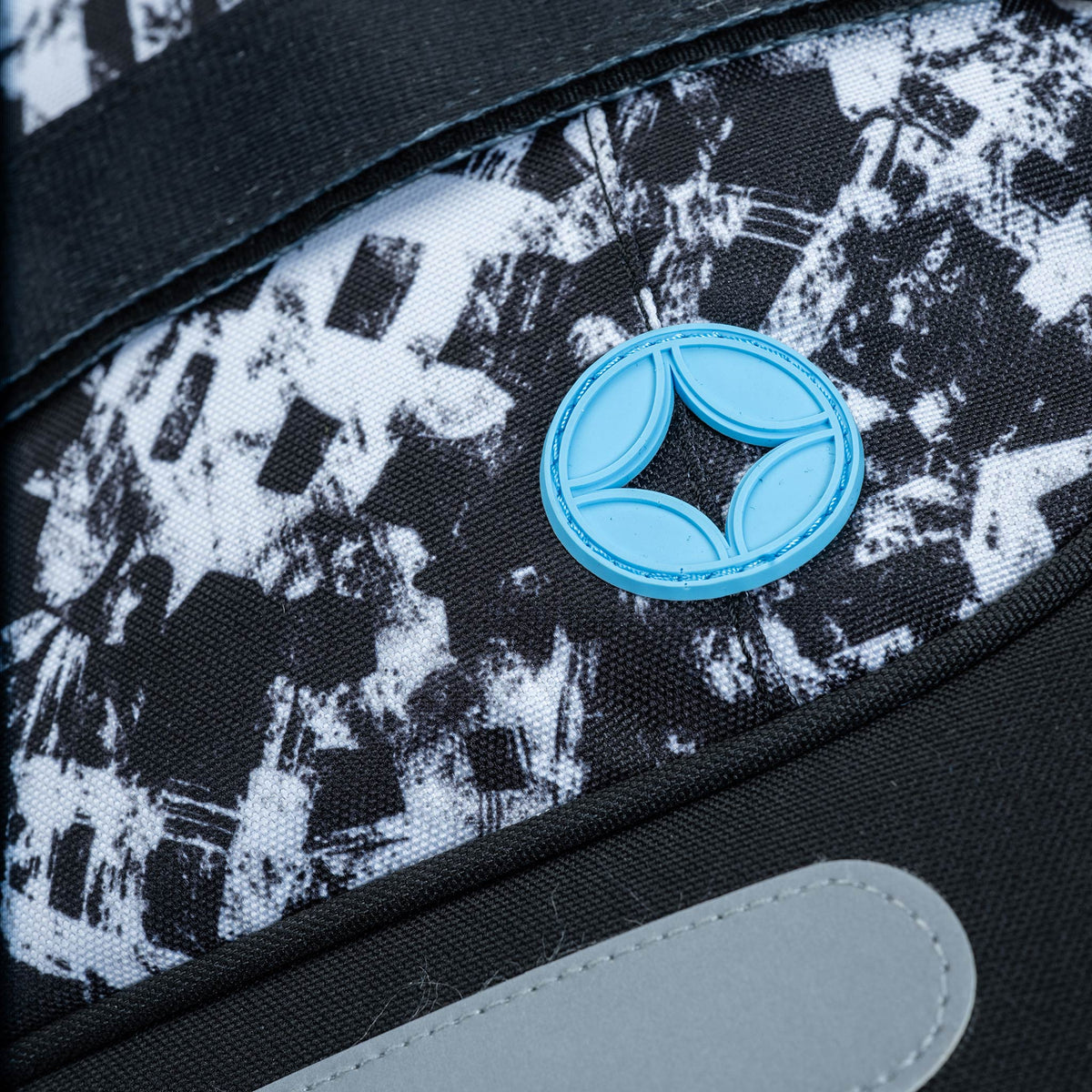 Bag close-up showing black and white abstract print panel with blue rubber circular logo badge and grey trim detail